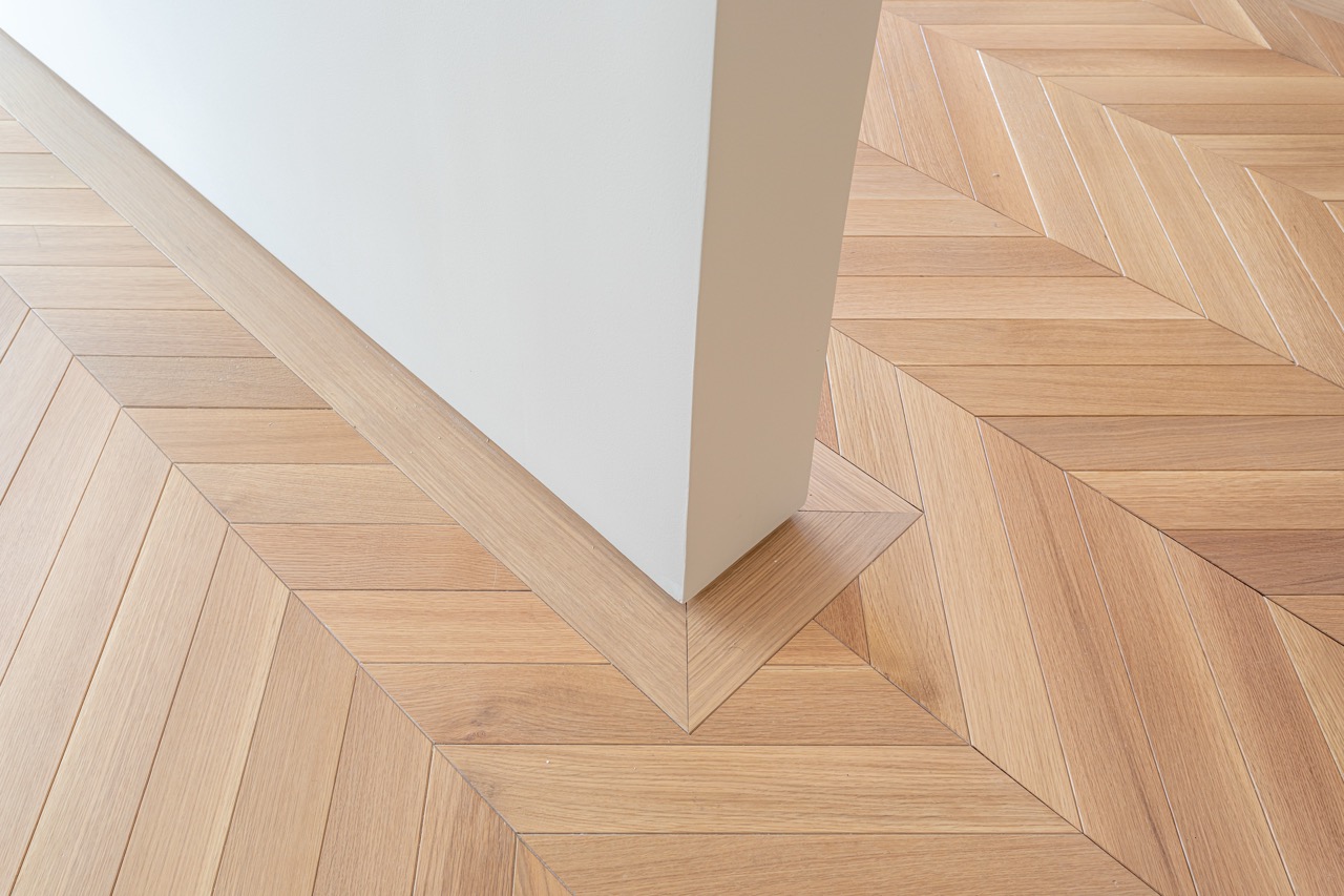 Minimalist interior architecture detail with herringbone wooden parquet floor pattern and clean white wall corner in modern apartment design. | Adobe Stock | nagelsphoto