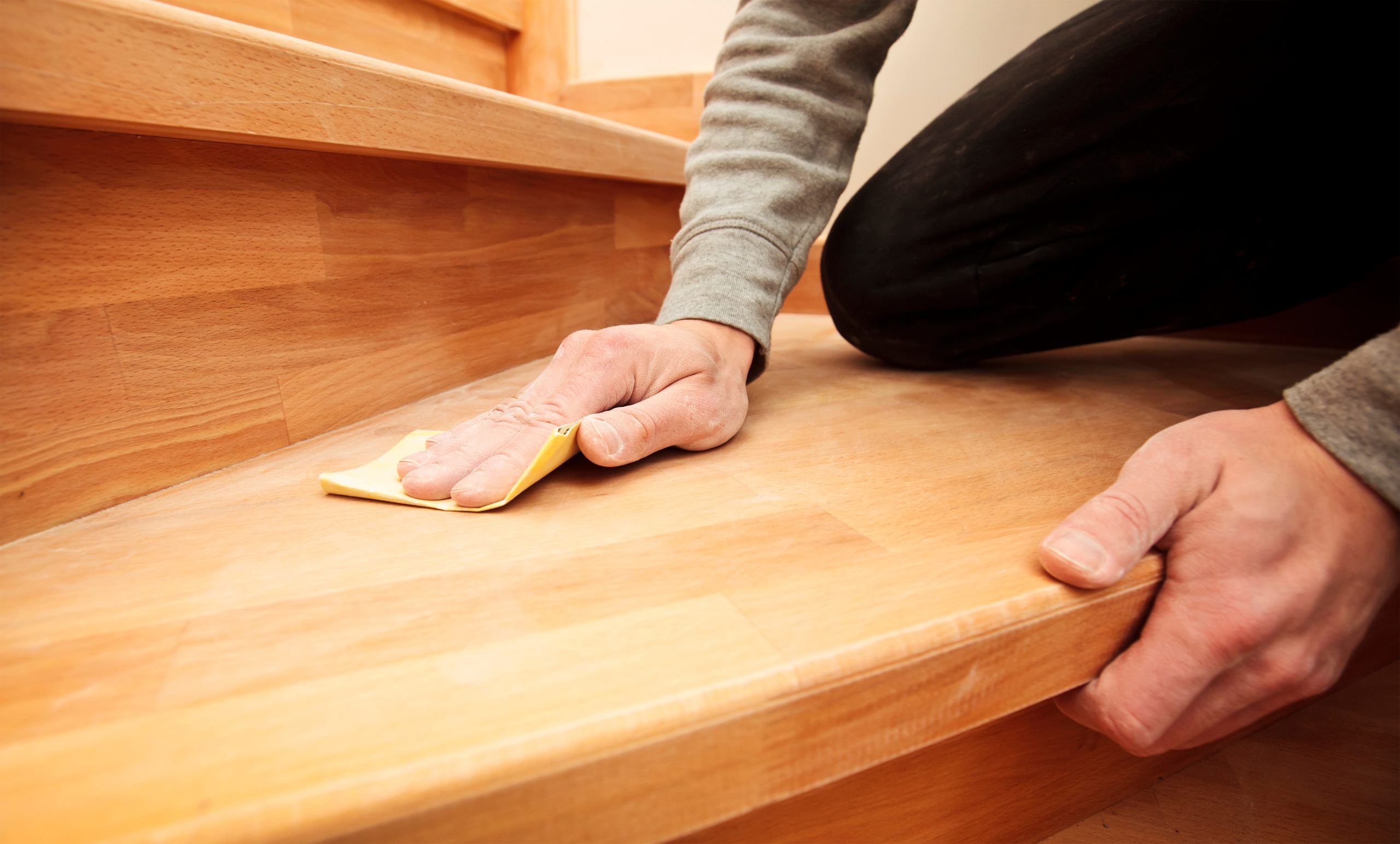 Professional finish carpenter repairing squeaky wooden stairs in a historic Massachusetts home.